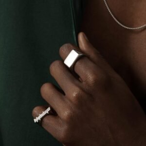 Sterling silver logo ring and square band set against emerald backdrop