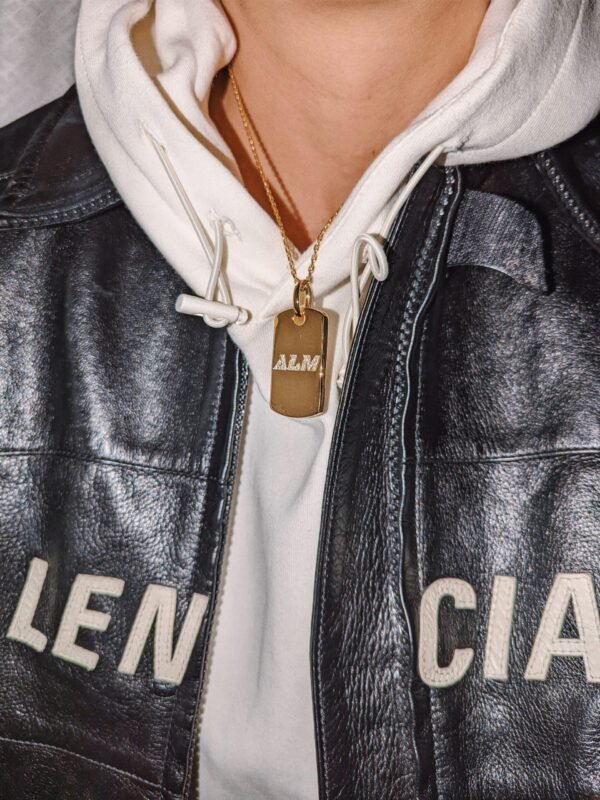 Gold plated dog tag with crystal "ALM" text, styled with white hoodie and leather jacket