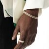 Gold diamond Cuban link bracelet and matching band ring on dark-skinned hand against white and green clothing