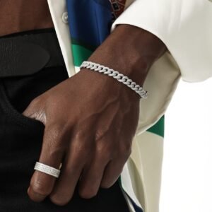 White gold diamond Cuban link bracelet and diamond band ring on dark-skinned hand with white and colored clothing backdrop