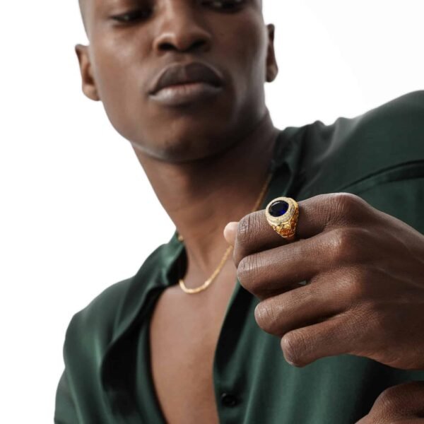 Gold sapphire ring with vintage design featured on dark-skinned model wearing emerald silk shirt and gold chain