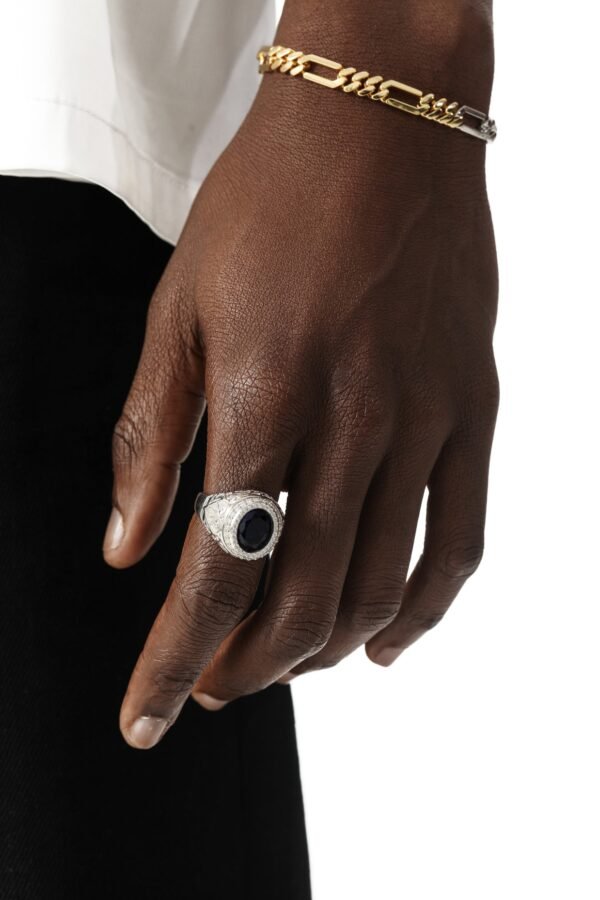 White gold sapphire ring paired with two-tone chain bracelet on dark-skinned hand against formal attire