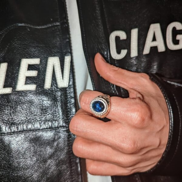 Gold sapphire ring with diamond halo shown against black leather jacket with white text detailing