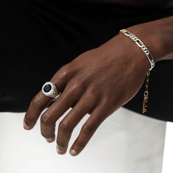 White gold antique-style sapphire ring and two-tone chain bracelet on dark-skinned hand against contrasting background