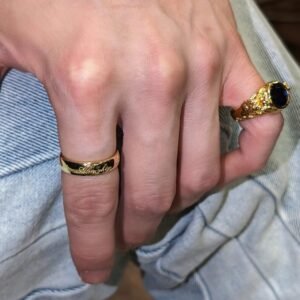 Gold plated band ring with engraved "Almighty" script worn with sapphire ring against denim background