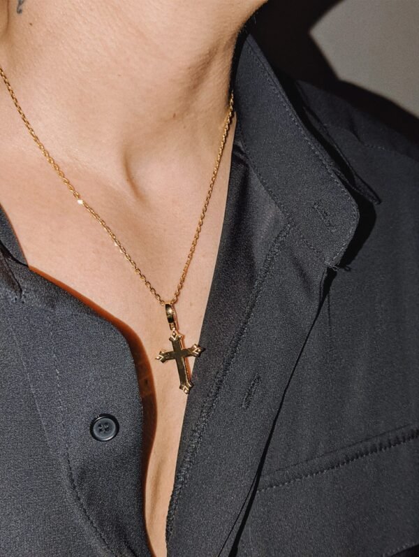 Gold plated polished cross pendant reverse side on fine chain with black shirt