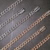 Multiple diamond-encrusted cuban link chains in white gold and 18k gold displayed on dark surface