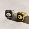 Side by side comparison of ghost signet rings in silver and gold finishes with black enamel detail