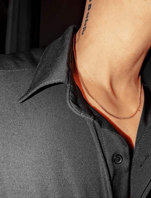 Close-up of gold round box chain necklace against black shirt