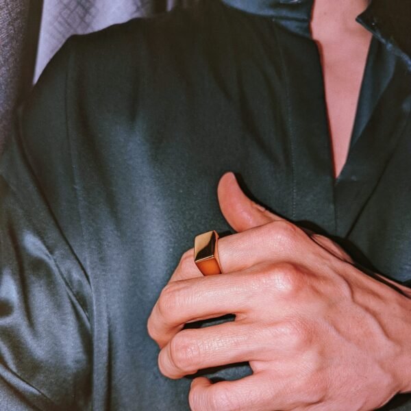 Gold square signet ring worn with black formal jacket against evening lighting