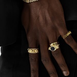 Gold rings and diamond Cuban bracelet styled on dark skin against black background