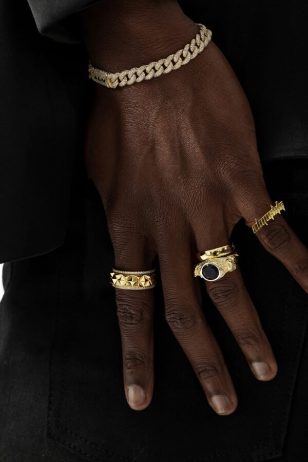 Gold rings and diamond Cuban bracelet styled on dark skin against black background