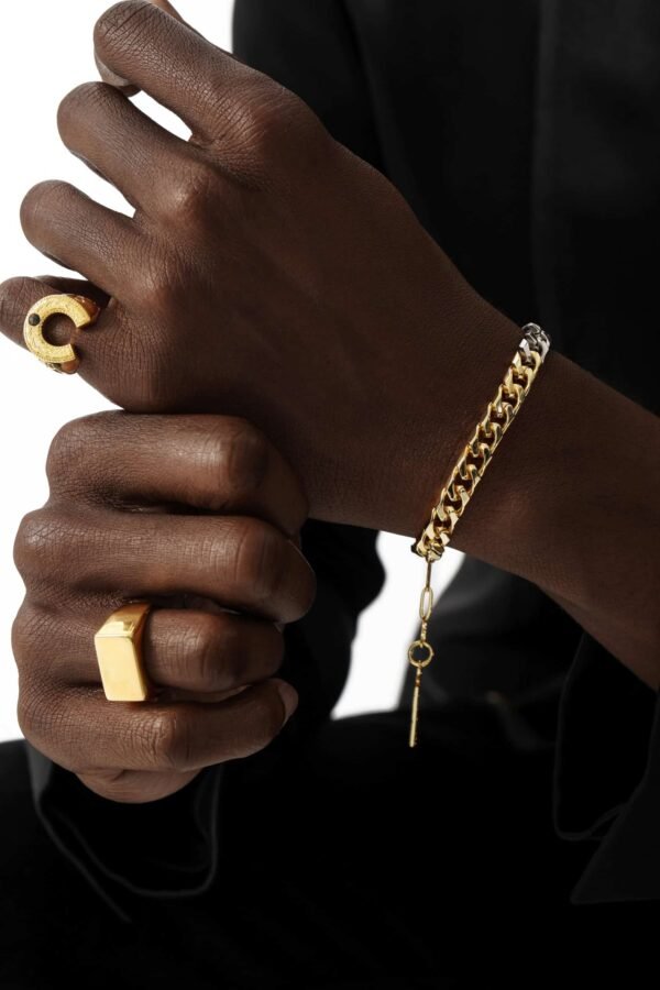 Gold rings paired with Cuban link bracelet, worn on dark skin against black clothing