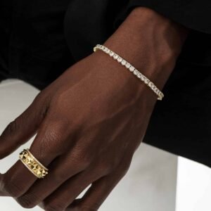 Gold plated tennis bracelet and textured ring worn on dark skin against black and white background