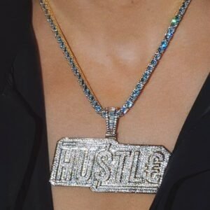 Gold HUSTLE pendant with cubic zirconia on matching tennis chain necklace in flash light