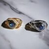 Gold and silver rings featuring leopard and tiger designs with blue sapphire stones on marble surface