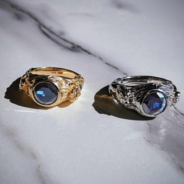 Gold and silver rings featuring leopard and tiger designs with blue sapphire stones on marble surface