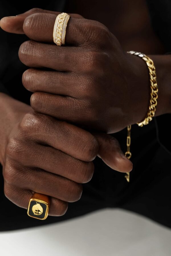 Gold diamond-set Cuban link spinner ring paired with square black enamel ghost ring on dark skin