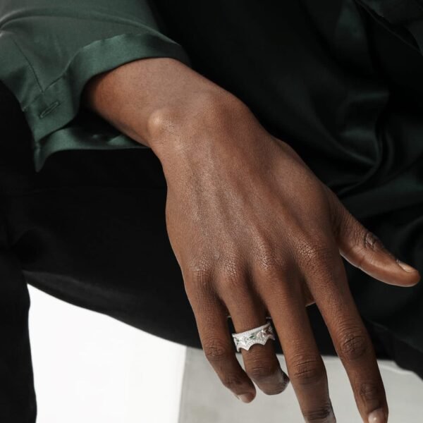 Silver crown ring with emeralds worn on dark skin tone against black and emerald green clothing