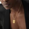 Gold-tone dog tag pendant with revolver design worn with black blazer