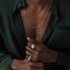 Model wearing white gold rings and round box chain with emerald green silk shirt