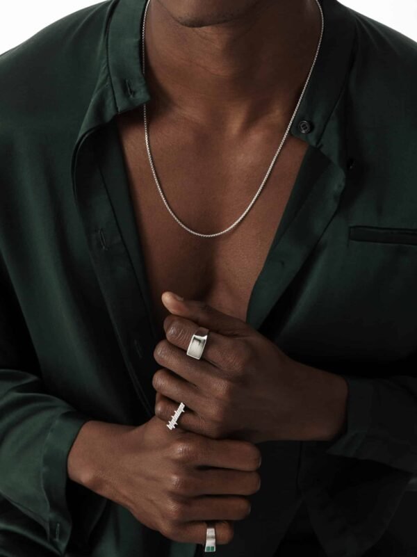 Model wearing white gold rings and round box chain with emerald green silk shirt