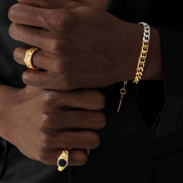 Gold sapphire rings paired with two-tone Cuban link bracelet on dark skin against black background