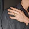 Gold shark jaw ring worn on hand resting against black shirt, partial tattoo visible