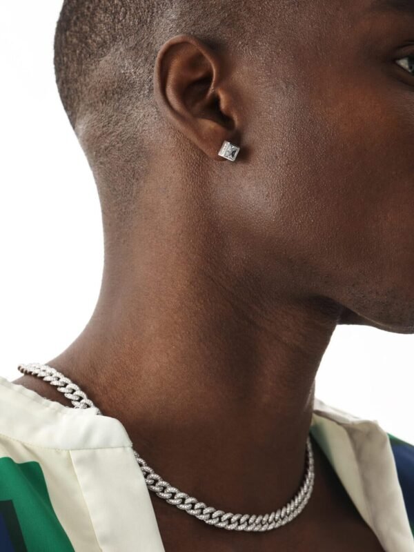 Profile view of silver pyramid stud earring and silver Cuban chain necklace on model