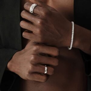 Silver studded band ring and tennis bracelet worn on dark skin against black background