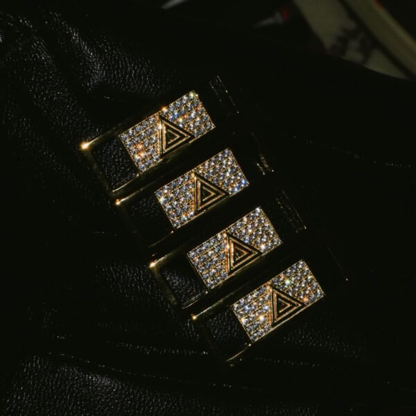 Four gold sneaker crowns with diamond-like stones on dark background